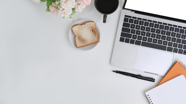 Vue ci-dessus bureau blanc avec ordinateur portable, ordinateur portable, pain et tasse à café.