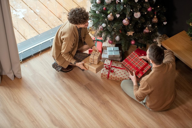 Vue ci-dessus d'un couple marié assis sur le sol et mettant des cadeaux dans de beaux emballages sous Noël...