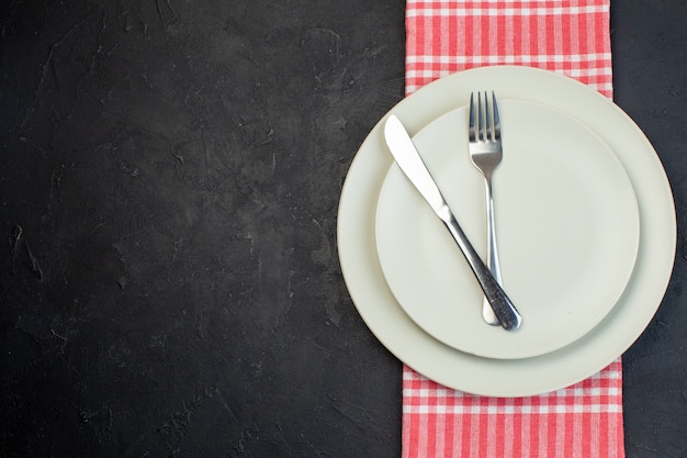 Vue ci-dessus des couverts en acier inoxydable sur des assiettes vides blanches sur une serviette rayée rouge sur le côté gauche sur fond noir avec espace libre