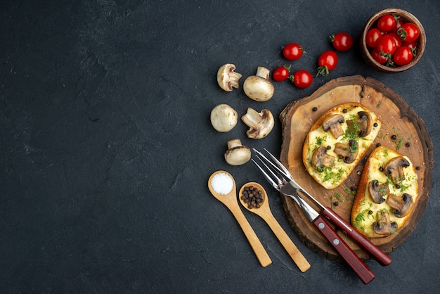 Vue ci-dessus d'une délicieuse collation avec des couverts de champignons sur une planche en bois et des légumes crus d'épices sur fond noir