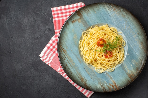 Vue ci-dessus de délicieux spagetti servis avec des tomates vertes sur une serviette rayée rouge sur le côté gauche sur fond noir