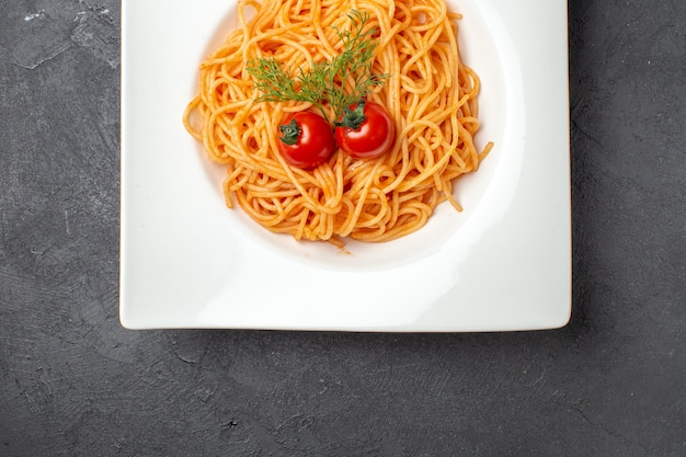 Vue ci-dessus de délicieux spagetty servi avec des tomates vertes sur une plaque carrée blanche sur fond noir