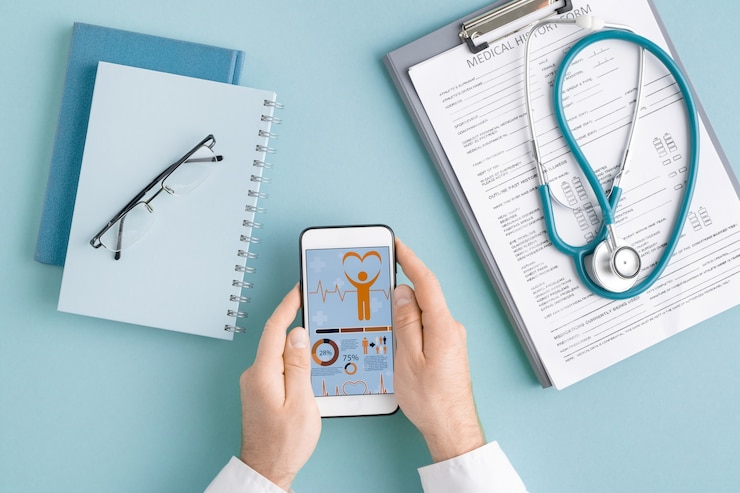Photo vue ci-dessus des mains du cardiologue avec smartphone faisant défiler les statistiques médicales en ligne parmi le document dans le presse-papiers et les cahiers