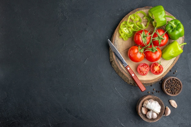 Vue ci-dessus de poivrons verts coupés entiers et de tomates fraîches couteau sur une planche à découper en bois sur le côté gauche sur une surface noire