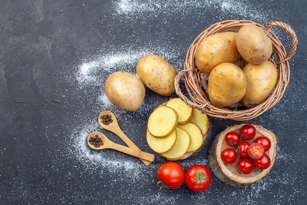 Photo vue ci-dessus de pommes de terre fraîches entières et hachées et de tomates sur planche de bois poivre sur le côté gauche sur fond de couleurs de mélange blanc noir