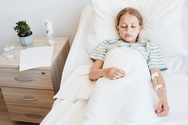 Vue ci-dessus portrait d'un enfant allongé dans un lit d'hôpital avec support en oxygène et perfusion IV, espace pour copie