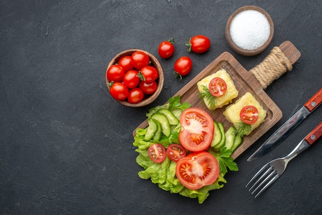 Vue ci-dessus des tomates fraîches coupées et du fromage de concombres sur des couverts en bois mis en sel sur une surface noire