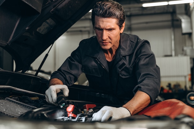 Vue en contre-plongée du mécanicien automobile sérieux se tenant près de la voiture cassée dans le service de réparation automobile au garage de service automobile. Notion d'automobiles