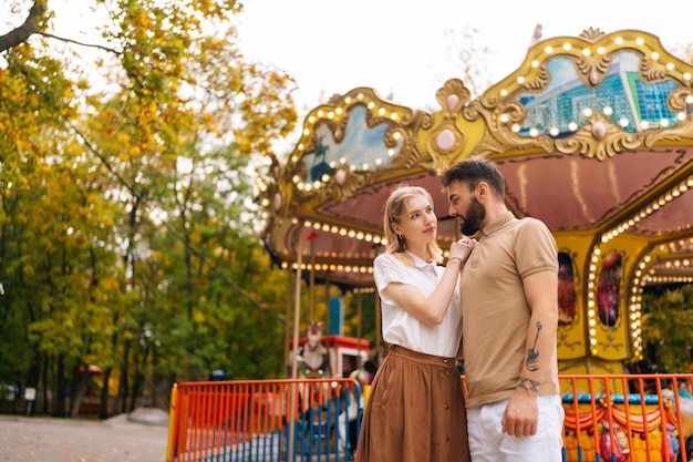 Vue en contre-plongée d'un jeune couple romantique amoureux debout embrassant dans un parc d'attractions sur fond de carrousel le jour d'été