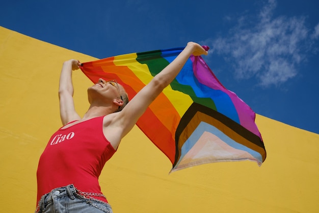 Vue en contre-plongée d'une personne non binaire joyeuse tenant et agitant un drapeau de fierté lgbtq à l'extérieur. Concept d'égalité et d'identité de genre.