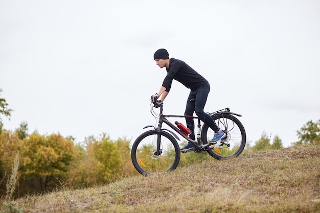 Vue côté, de, cycliste, équitation, vtt, descente, sports extrêmes, sur, vélo, dehors, jeune, sportif, porter, noir, sportsuit, et, casquette