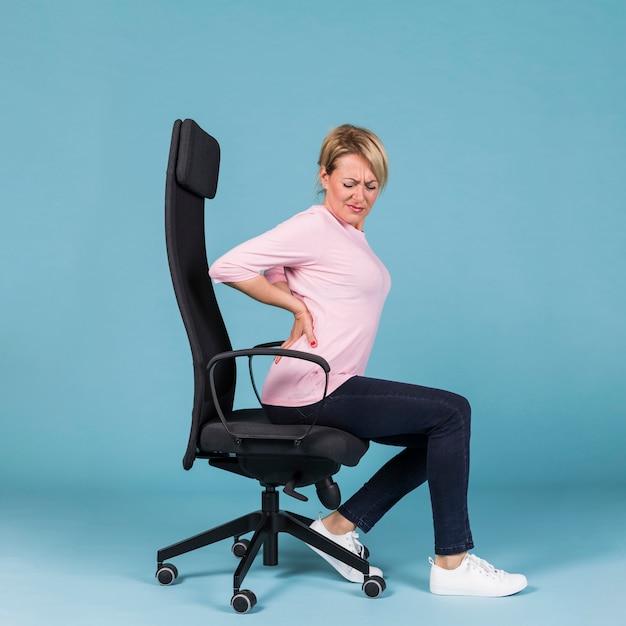 Vue de côté d'une femme assise sur une chaise, souffrant de maux de dos