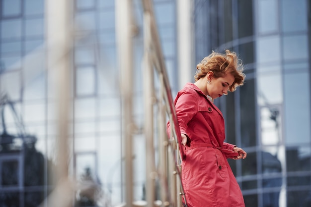 Vue de côté. Jolie femme adulte en manteau rouge chaud se promène dans la ville à son heure du week-end