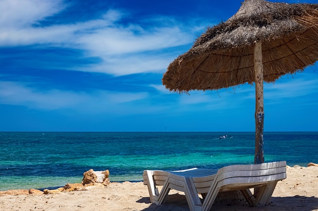 Une vue sur la côte méditerranéenne avec de l'eau de bouleau sur laquelle se trouvent une chaise longue et un parasol. Repos à la mer sur l'île de Djerba, Tunisie