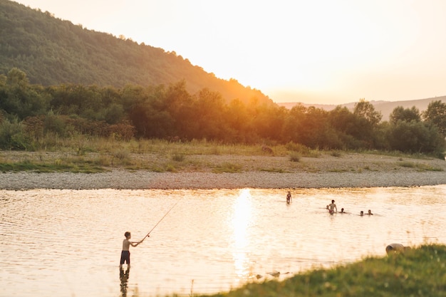 Vue sur le coucher du soleil dans les montagnes au-dessus des personnes nageant dans la rivière l'heure d'été