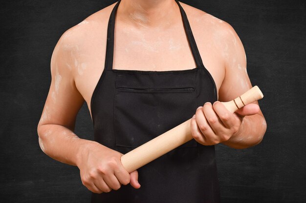 Vue coupée d'un chef cuisinier masculin avec une épingle à rouleaux sur fond noir tenant une éping le roulant pour la pâte