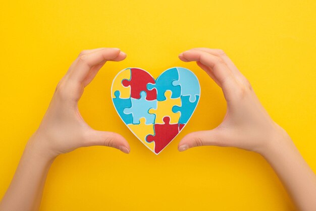 vue coupée de mains féminines avec un cœur de puzzle sur jaune pour la Journée mondiale de la sensibilisation à l'autisme