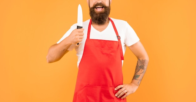 Vue de la culture de l'homme heureux tenant un couteau de cuisinier portant un tablier rouge cuisinier sur fond jaune