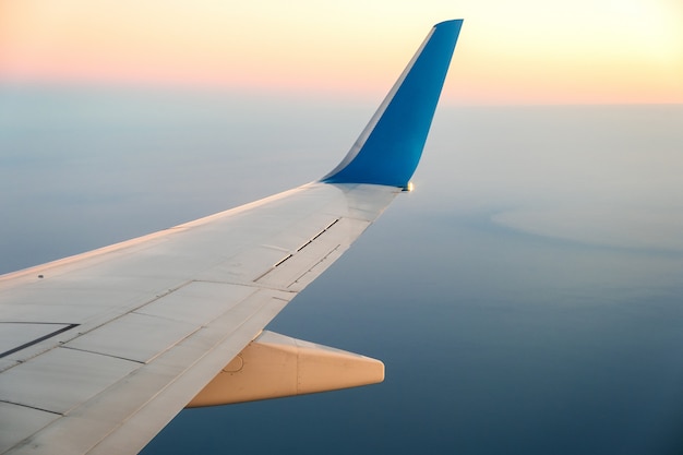 Vue depuis l'avion sur l'aile blanche de l'avion survolant le paysage océanique en matinée ensoleillée. Concept de voyage et de transport aérien.