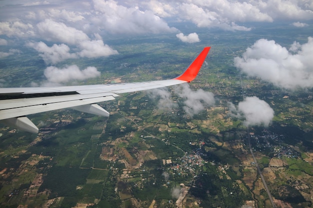 Vue depuis la fenêtre de l&#39;avion avec l&#39;aile de l&#39;avion, le ciel bleu, les nuages ​​blancs et les terres vertes.