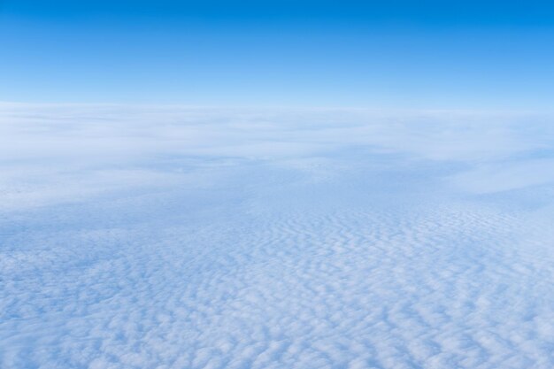 La vue depuis la fenêtre de l'avion de nuages bouclés denses et de la stratosphère bleue