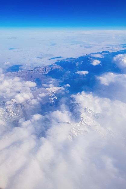 Vue depuis la fenêtre de l'avion vers le ciel bleu et les sommets enneigés dans les nuages blancs