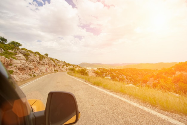 La vue depuis la fenêtre de la voiture sur le chemin et les montagnes au coucher ou au lever du soleil