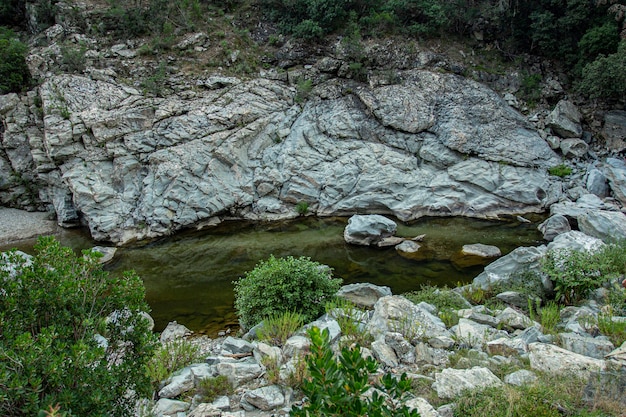 Vue depuis le fond du ruissellement naturel de Sa Stiddiosa : une paroi rocheuse recouverte de végétation laisse tomber l'eau à travers les parois et les ondulations entre les rochers.