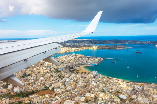 Vue depuis le hublot d'un avion de passagers sur la côte de Malte avec des maisons typiques.