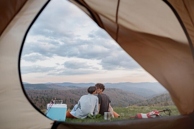 Vue depuis l'intérieur de la tente sur un magnifique paysage de montagnes et couple s'embrassant Amour et voyage