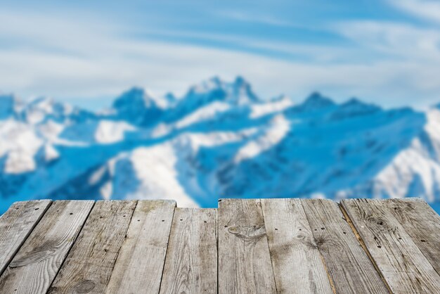 Vue depuis la table de terrasse en bois vide pour les montagnes d'hiver ensoleillées en bokeh