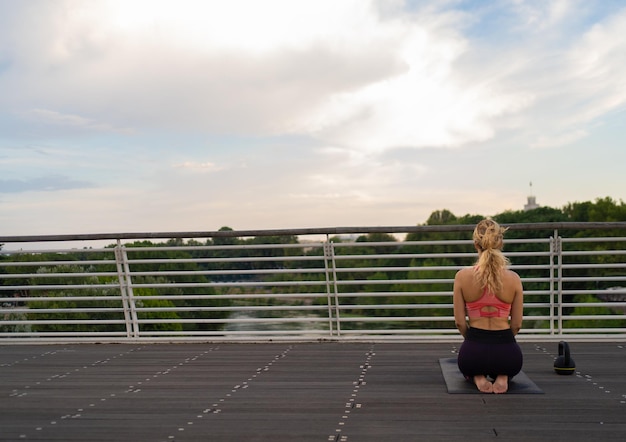 Vue de derrière de Girl with smartwatch réalisant le yoga au milieu de la ville reflétant