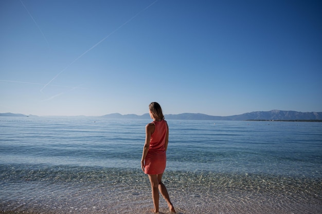 Vue de derrière d'une jeune femme debout à la hauteur de la cheville en mer claire