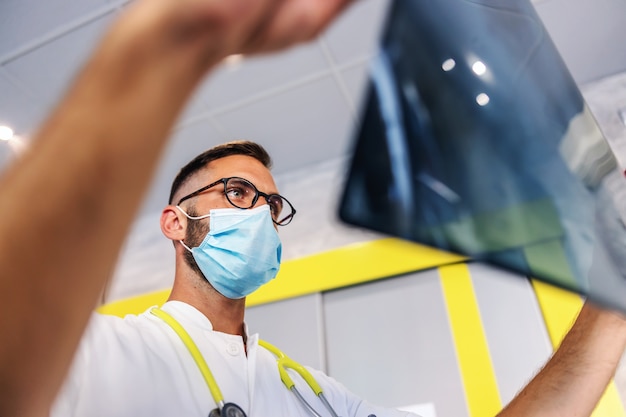 Vue de dessous du jeune médecin dédié tenant la radiographie des poumons du patient et en la regardant.