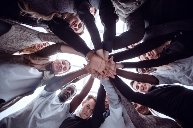 Vue de dessous groupe de jeunes heureux faisant une tour de leurs mains