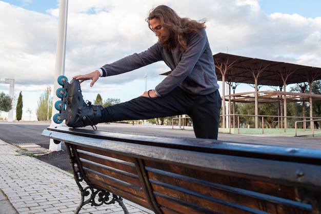 Vue en dessous, de, jeune, cool, sportswear, à, patins a roulettes, étirer, sur, banc, dans, parc