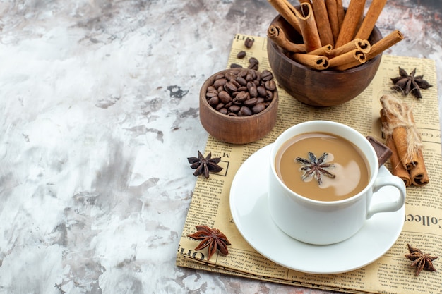 vue de dessous tasse de café avec des grains de café torréfiés à l'anis dans un bol en bois bâtons de cannelle au chocolat attachés avec de l'anis de corde sur du papier journal sur une table avec un espace libre