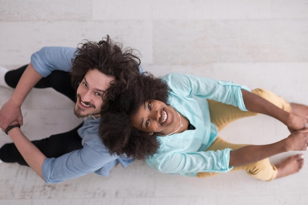 vue de dessus 0f Enthousiaste jeune couple multiethnique assis dos à dos sur le sol et souriant