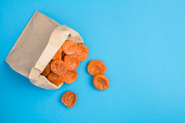 Vue de dessus des abricots secs dans un sac en papier sur le bleu