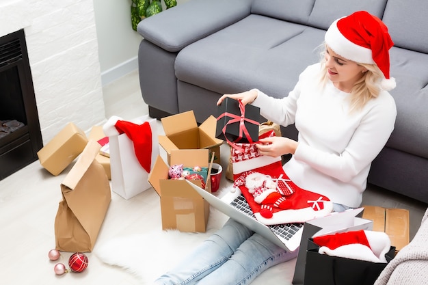 Vue de dessus des achats en ligne de Noël. Acheteur féminin avec ordinateur portable, copiez l'espace à l'écran. Une femme prend un café, achète des cadeaux, se prépare pour la veille de Noël, assise parmi des coffrets cadeaux et des colis. Soldes vacances d'hiver