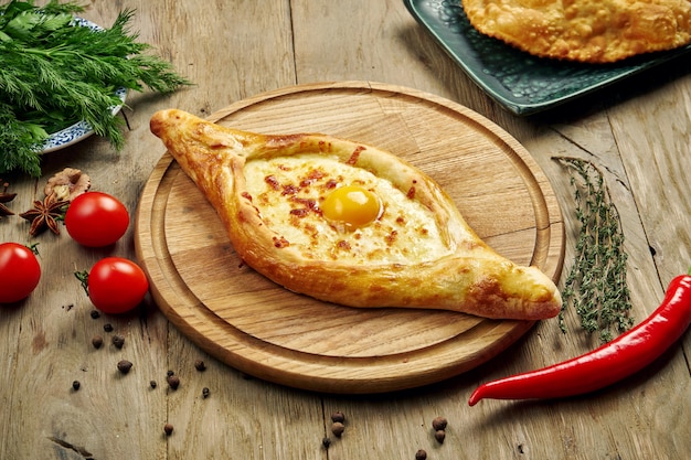 Vue de dessus sur l'adjarian Khachapuri traditionnel savoureux - tarte au four ouverte avec du fromage de sel fondu (suluguni) et du jaune d'oeuf sur un plateau en bois. Cuisine géorgienne traditionnelle