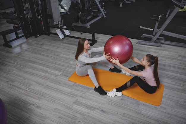 Vue de dessus d'une adolescente qui s'entraîne avec un entraîneur de fitness à la salle de sport faisant des redressements assis avec un ballon en forme