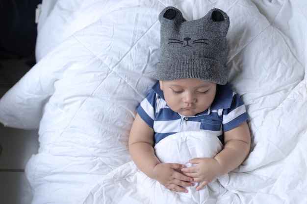 Vue de dessus de l'adorable petit garçon portant un chapeau mignon dormant en toute sécurité sur le lit dans un drap blanc