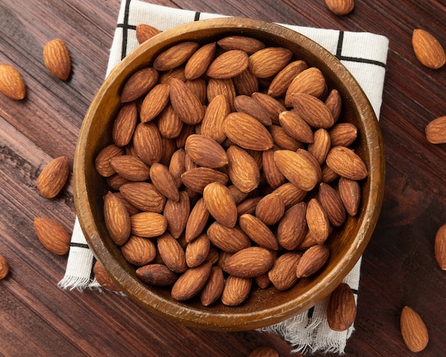 Vue de dessus des amandes dans un bol en bois sur la table, mise à plat, collation saine, nourriture végétarienne.