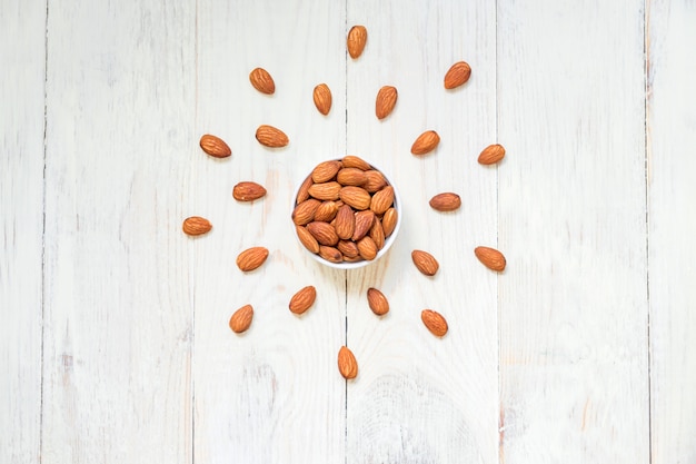 Vue de dessus d'amandes grillées dans un bol en porcelaine blanche sur une table en bois blanche