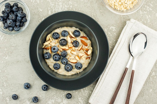 Vue de dessus d'une assiette en céramique sombre avec de la farine d'avoine, des bleuets mûrs et des amandes. délicieux petit déjeuner sain. fond de béton gris.