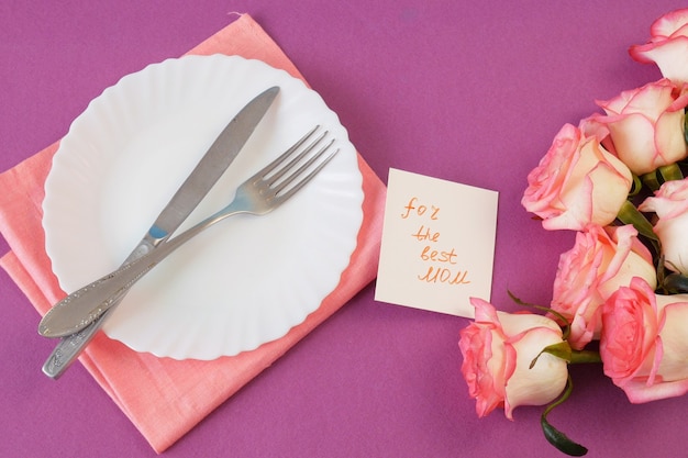 Vue de dessus de l'assiette vide blanche et de nombreuses roses roses et carte de fête des mères