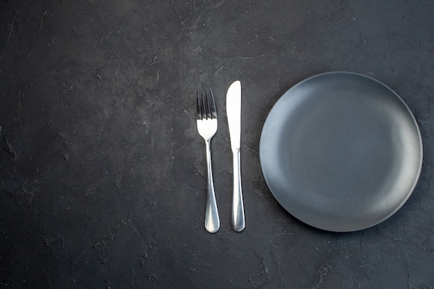 Vue de dessus de l'assiette vide de couleur gris foncé et des couverts en acier inoxydable sur le côté gauche sur fond noir avec espace libre