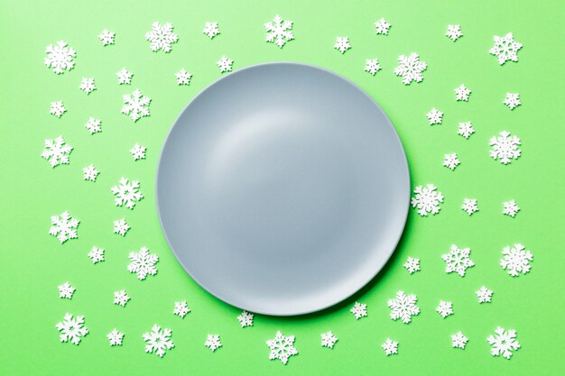 Vue de dessus d'une assiette vide entourée de flocons de neige sur fond coloré. Dîner du nouvel an