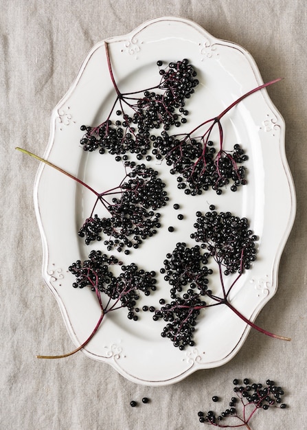 Vue de dessus d'une assiette vintage blanche avec des grappes de baies de sureau noires mûres sur une nappe en lin